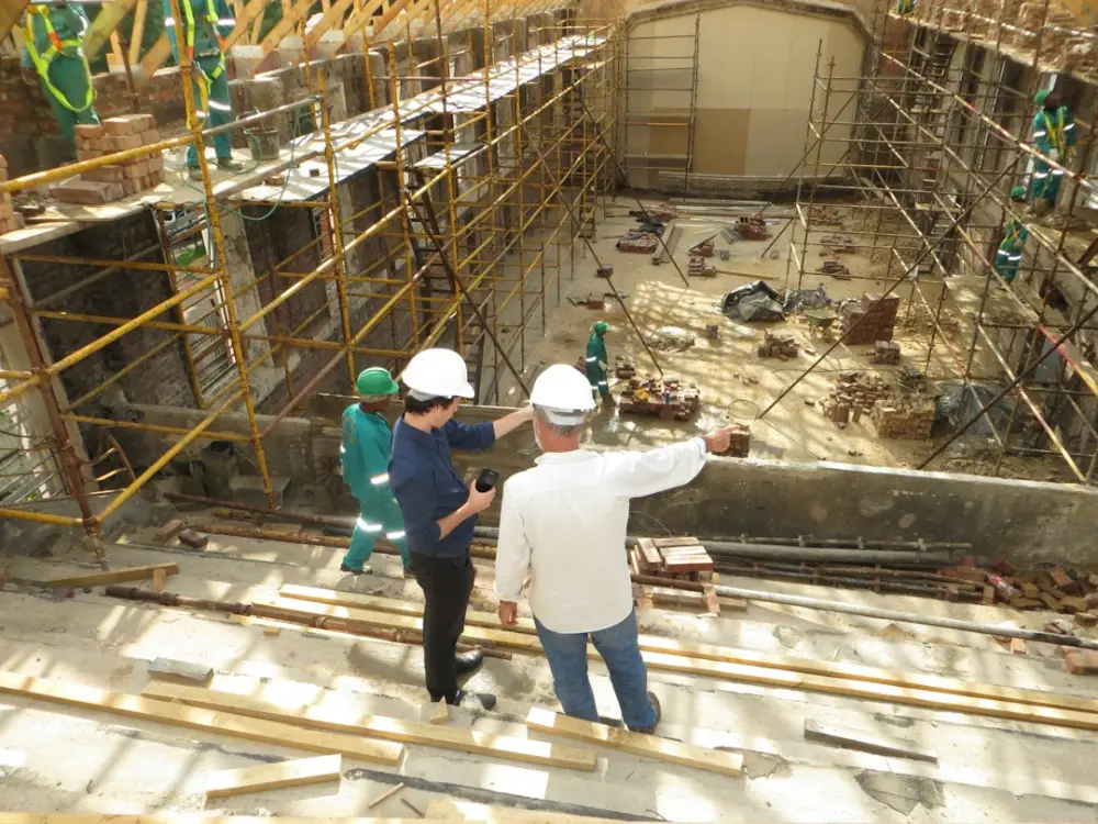 Two men in hard hats pointing at a construction site with scaffolding, illustrating construction management NVQ